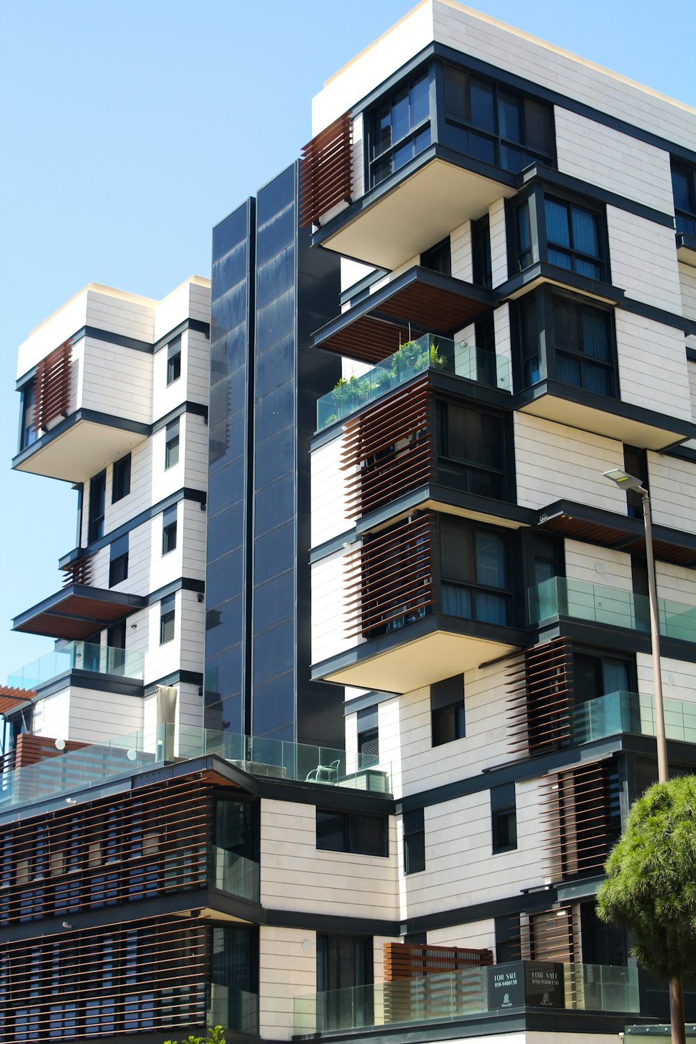 A modern condominium building with tiered balconies against a clear sky.